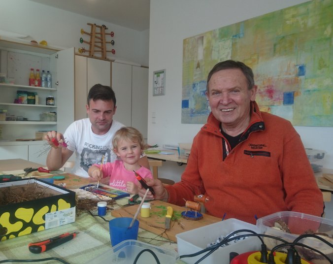 Zwei Väter sitzen mit einem Kind an einem Tisch und basteln.
