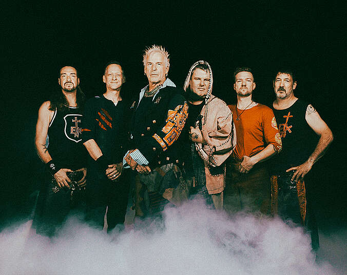 Sechs Männer nebeneinander stehend in Nebel, gekleidet in mittelalterlicher Rocker-Kleidung.