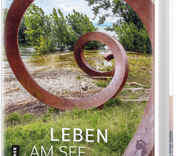 Buchcover: Uferlandschaft am See mit Bewuchs. Eine verwitterte große Spirale steht als Metallskulptur in der Landschaft.