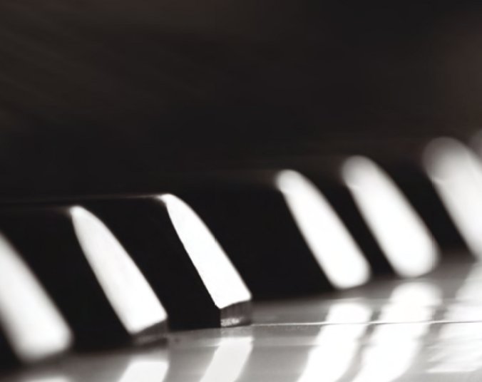 Nahaufnahme eines kleinen Ausschnitts einer Klaviertastatur. Es sind die Köpfe von sechs schwarzen Tasten zu erkennen, darunter verschwommen weiße Tasten.