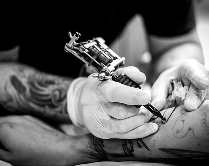 Schwarz-Weiß-Bild, Nahaufnahme/Bildausschnitt: Ein Arm wird tatowiert