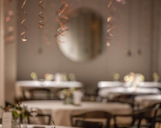 Festlich geschmückter Raum mit goldenen Papierschlangen im Vordergrund, verschwommen im HIntergrund festlich gedeckte Tische.