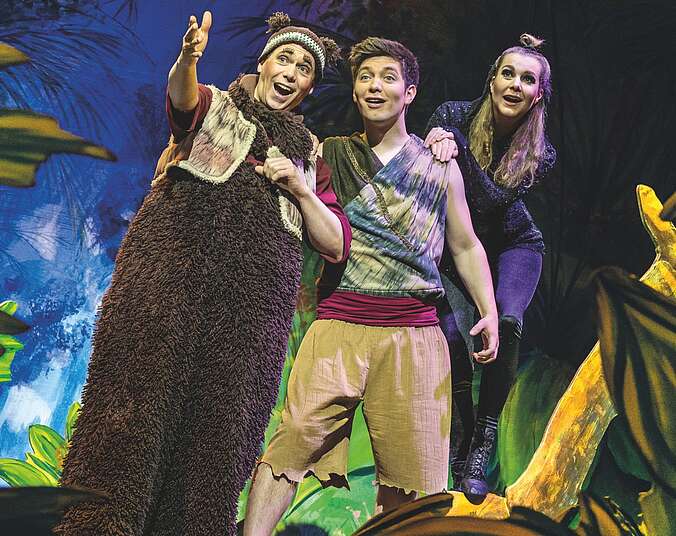 Drei junge Menschen stehen in einer Gruppe zusammen: zwei Männer, eine Frau. Der Mann links trägt ein Fellkostüm und eine Strickmütze mit Bärenohren, der Junge in der Mitte trägt aberissene knielange Short. Die Frau trägt enge schwarze Kleidung.