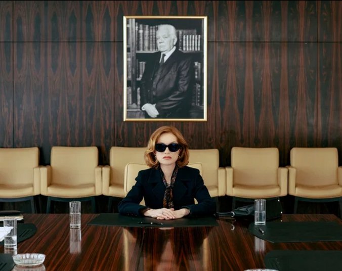 Frau mit Sonnenbrille sitzt an großem Tisch. (Foto: Neue Visionen. Screenshot Veranstalter Cineplex)