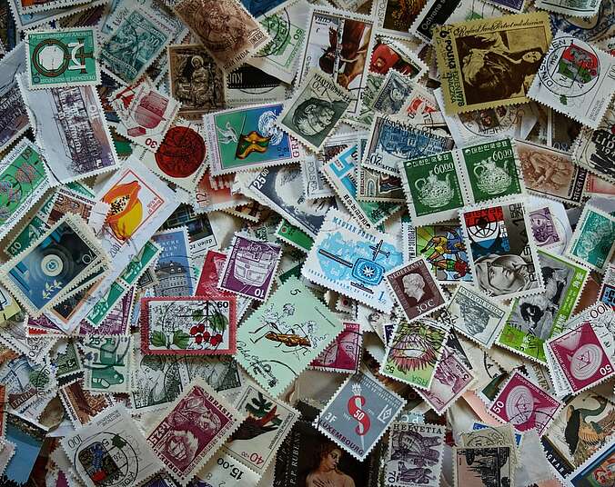 Viele bunte, internationale Briefmarken liegen auf der gesamten Bildfläche gemischt durcheinander.