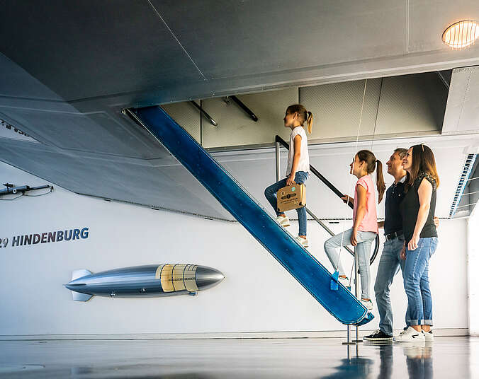 Drei Menschen steigen in einen Zeppelin ein