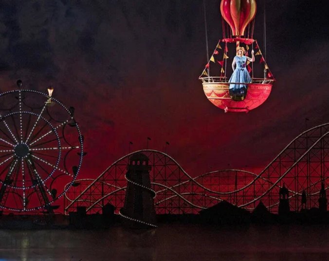 Frau in Ballongondel über Rummelplatzbühnenbild. (Foto: 2026 LEONINE Distribution GmbH. Screenshot Veranstalter Cineplex)