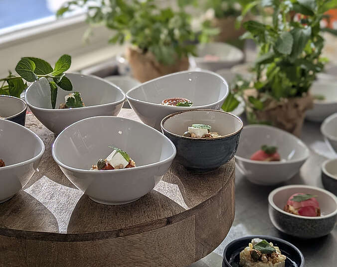 Verschiedene Schälchen mit Desserts auf einem Tisch mit Pflanzen im Hintergrund.